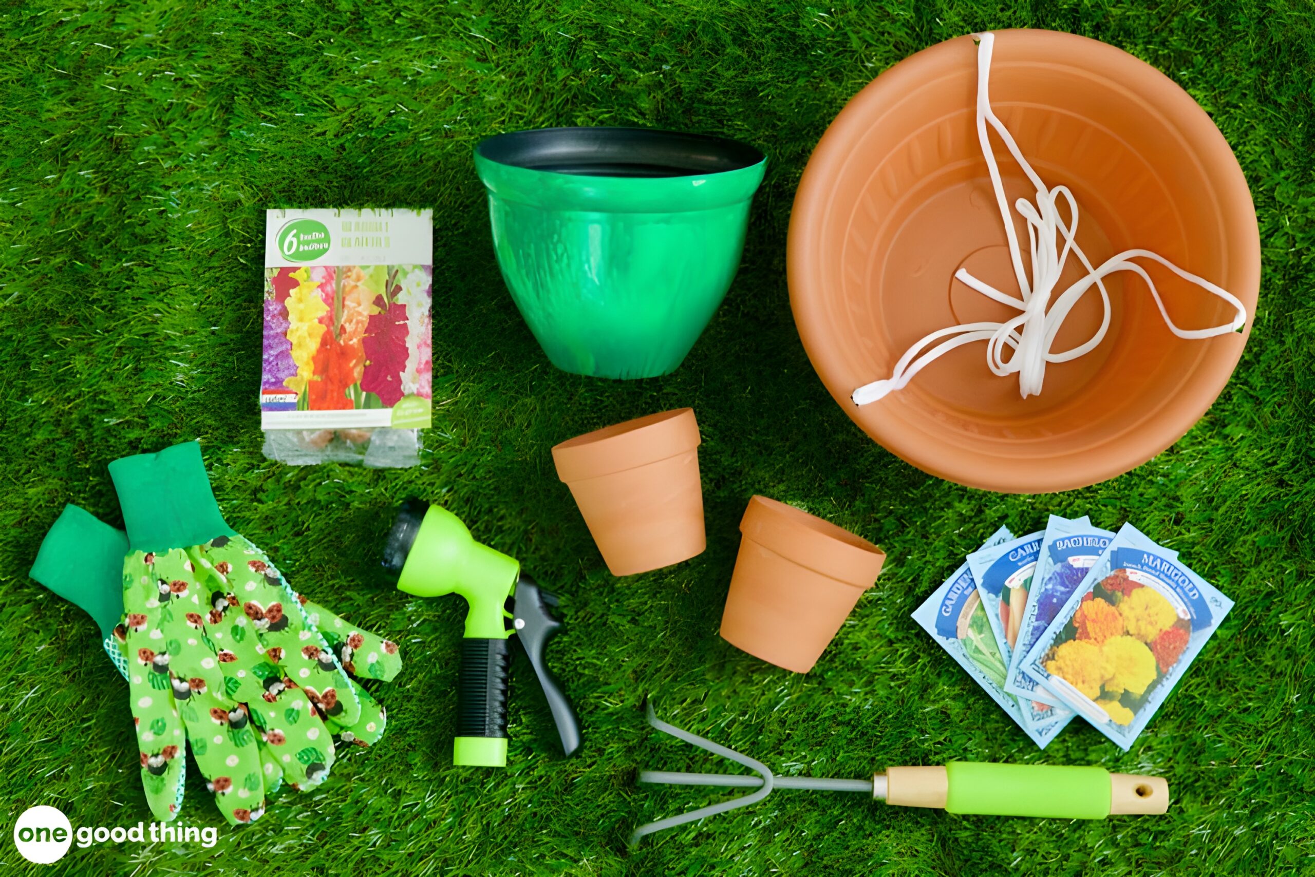 summer-dollar-store4 Assorted dollar store gardening tools, pots, gloves, a hose nozzle, seed packets, and a box of seeds are arranged on grass.