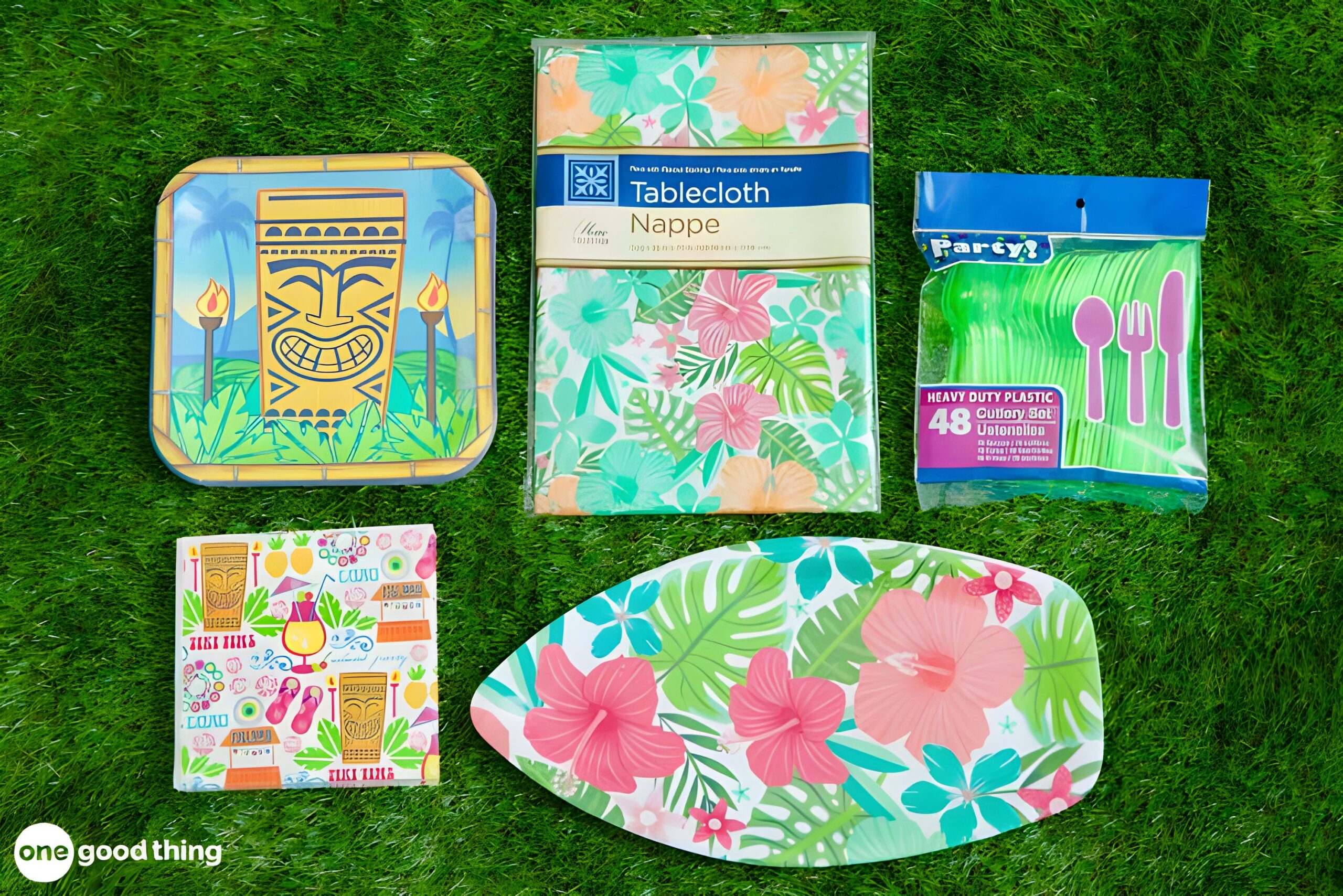 summer-dollar-store7 Assorted tropical-themed party supplies, including plates, napkins, a tablecloth, and green plastic cutlery from the dollar store, all arranged on green grass.