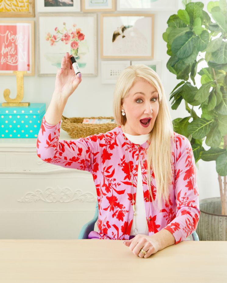 soothe aches and pains_8 A woman in a red floral sweater sits at a desk, holding a glue stick aloft in her right hand, with her mouth open as if speaking or surprised—perhaps discussing how she manages everyday aches while staying creative.