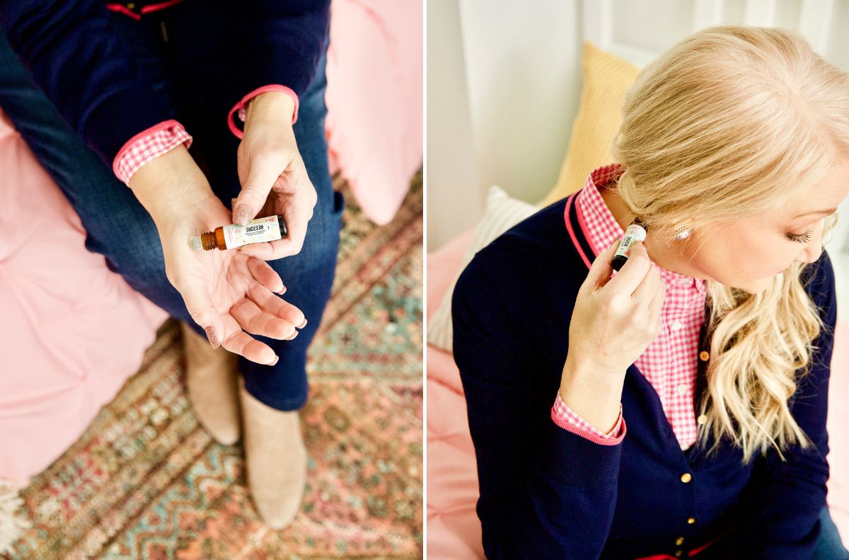 soothe aches and pains_2 A person applies essential oil to their wrist and behind their ear while sitting on a bed, seeking relief from everyday aches.