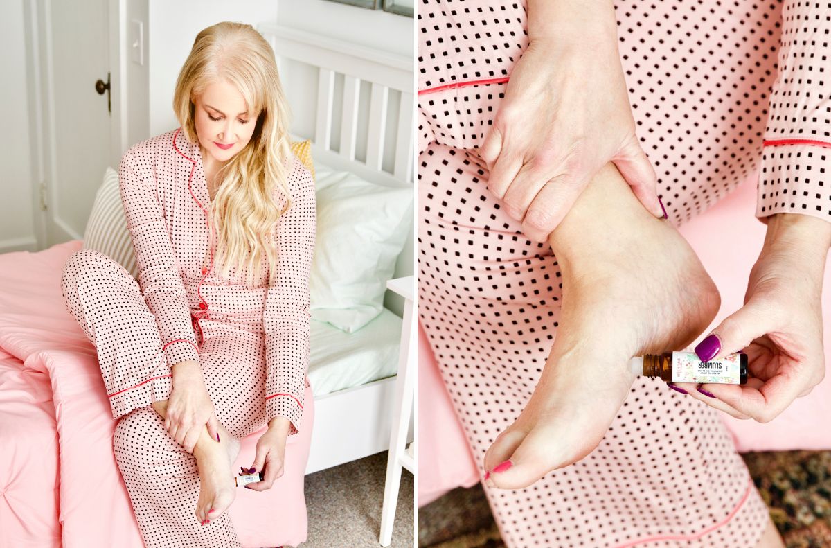 soothe aches and pains_5 A person in pink polka dot pajamas applies cream and oil to their feet while sitting on a bed and holding their ankle, soothing everyday aches with gentle care.