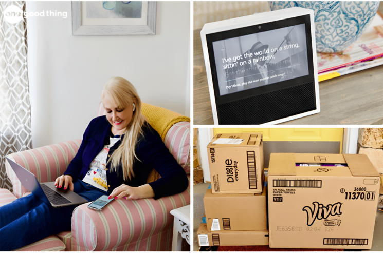 A woman uses a phone and laptop in an armchair; a smart display shows song lyrics, while boxes—ready to help her save money on Amazon—are stacked near the door.